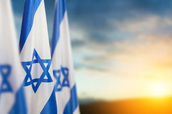 Israel flags with a star of David over cloudy sky background on sunset. Patriotic concept about Israel with national state symbols. Banner with place for text.