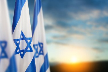 Israel flags with a star of David over cloudy sky background on sunset. Patriotic concept about Israel with national state symbols. Banner with place for text.