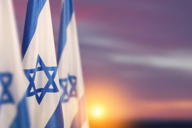 Israel flags with a star of David over cloudy sky background on sunset. Patriotic concept about Israel with national state symbols. Banner with place for text.