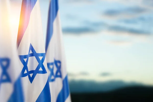 Israel flags with a star of David over cloudy sky background on sunset. Patriotic concept about Israel with national state symbols. Banner with place for text.