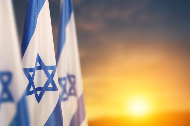 Israel flags with a star of David over cloudy sky background on sunset. Patriotic concept about Israel with national state symbols. Banner with place for text.