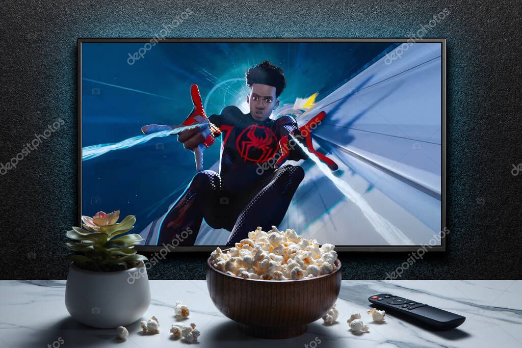 TV screen playing Spider-Man Across the Spider-Verse trailer or movie. TV with remote control, popcorn bowl and home plant. Astana, Kazakhstan - May 15, 2023.