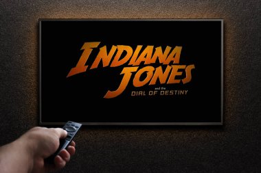 TV ekranında Indiana Jones ve Kaderin Kaderi karavanı ya da filmi oynanıyor. Adam uzaktan kumandayla televizyonu açıyor. Astana, Kazakistan - 15 Mayıs 2023.