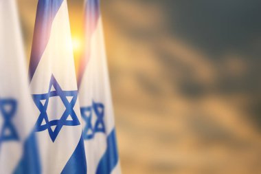 Israel flags with a star of David over cloudy sky background on sunset. Patriotic concept about Israel with national state symbols. Banner with place for text.