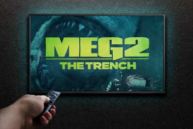 Meg 2 The Trench fragmanı ya da film. Adam uzaktan kumandayla televizyonu açıyor. Astana, Kazakistan - 2 Temmuz 2023.