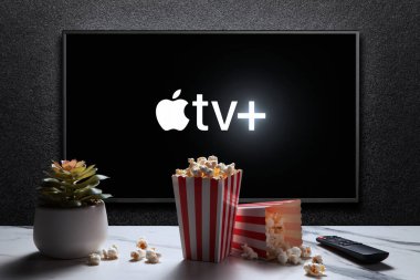 Apple TV plus logo on TV with popcorn boxes, reomote control and home plant on the table. Apple TV plus is an American subscription streaming service. Astana, Kazakhstan - July 21, 2023.