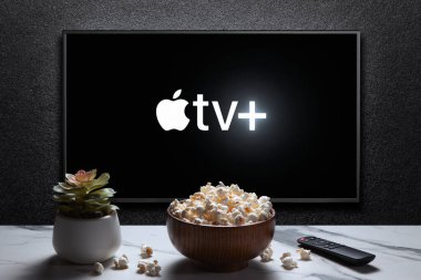 Apple TV artı TV 'de patlamış mısır kasesi, uzaktan kumanda ve masada ev bitkisi. Apple TV + bir Amerikan abonelik yayın hizmetidir. Astana, Kazakistan - 21 Temmuz 2023.