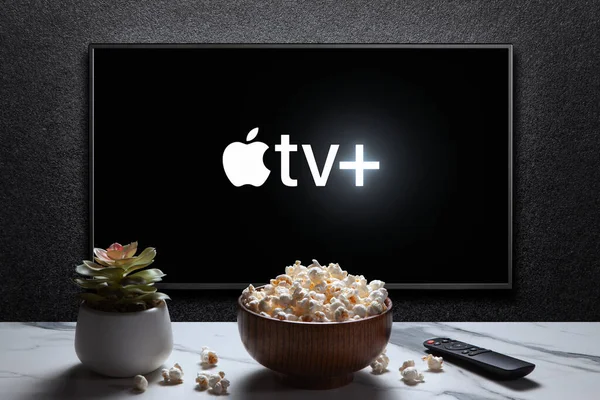 stock image Apple TV plus logo on TV with popcorn bowl, reomote control and home plant on the table. Apple TV plus is an American subscription streaming service. Astana, Kazakhstan - July 21, 2023.