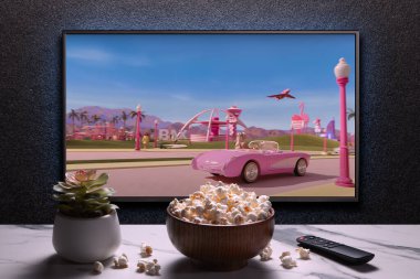 TV screen playing Barbie trailer or movie. TV with remote control, popcorn bowl and home plant. Astana, Kazakhstan - July 2, 2023. clipart