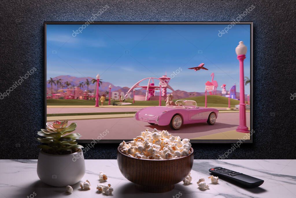 TV screen playing Barbie trailer or movie. TV with remote control, popcorn bowl and home plant. Astana, Kazakhstan - July 2, 2023.