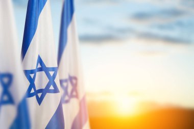 Israel flags with a star of David over cloudy sky background on sunset. Patriotic concept about Israel with national state symbols. Banner with place for text.
