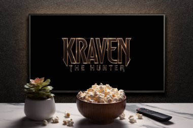 Avcı Kraven ya da TV ekranındaki film. Uzaktan kumandalı televizyon, patlamış mısır kasesi ve ev bitkisi. Astana, Kazakistan - 8 Eylül 2023.