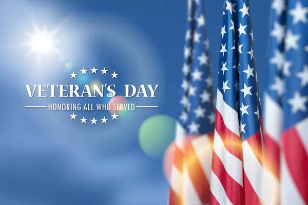 American flags with Text Veterans Day Honoring All Who Served on blue sky background. American holiday banner.