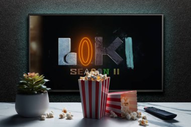 Amerikan televizyon dizisi Loki fragmanı ya da TV ekranındaki film. Uzaktan kumandalı televizyon, patlamış mısır kutuları ve ev bitkisi. Astana, Kazakistan - 5 Ekim 2023.