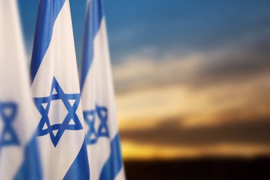 Israel flags with a star of David over cloudy sky background on sunset. Patriotic concept about Israel with national state symbols. Banner with place for text.