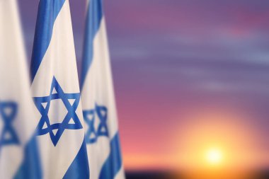 Israel flags with a star of David over cloudy sky background on sunset. Patriotic concept about Israel with national state symbols. Banner with place for text.