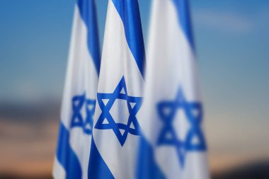 Israel flags with a star of David over cloudy sky background on sunset. Patriotic concept about Israel with national state symbols. Banner with place for text.