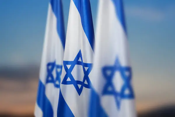 stock image Israel flags with a star of David over cloudy sky background on sunset. Patriotic concept about Israel with national state symbols. Banner with place for text.