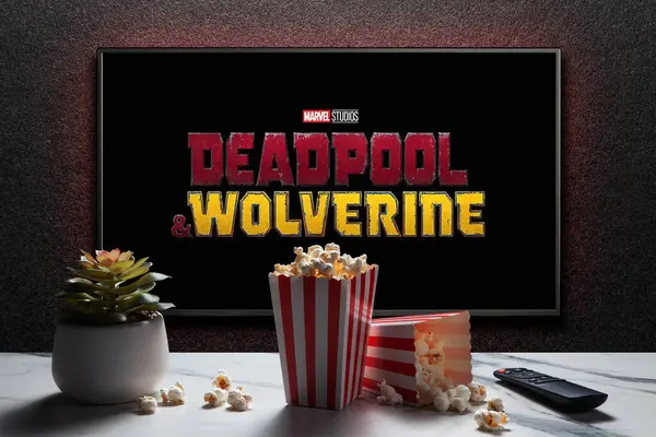 stock image Wolverine and Deadpool trailer or movie on TV screen. TV with remote control, popcorn boxes and home plant. Astana, Kazakhstan - July 31, 2024.