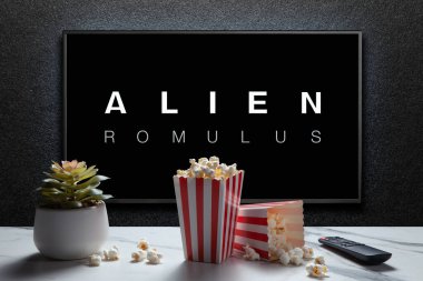 Alien Romulus trailer or movie on TV screen. TV with remote control, popcorn boxes and home plant. Astana, Kazakhstan - July 31, 2024. clipart