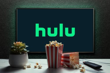 Televizyonda patlamış mısır kutuları, uzaktan kumanda ve masada ev bitkisi olan Hulu logosu. Hulu, Amerika 'da yayın yapan bir medya hizmetidir. Astana, Kazakistan - 23 Kasım 2024.