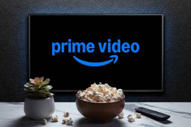TV 'de patlamış mısır kasesi, uzaktan kumanda ve masada ev bitkisi olan Amazon Prime Video logosu. Amerikan aboneliği medya hizmeti. Astana, Kazakistan - 23 Kasım 2024.