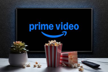TV 'de patlamış mısır kutuları, uzaktan kumanda ve masada ev bitkisi olan Amazon Prime Video logosu. Amerikan aboneliği medya hizmeti. Astana, Kazakistan - 23 Kasım 2024.