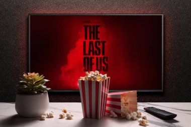 TV ekranında The Last of Us 2. Sezon fragmanı ya da film gösteriliyor. Uzaktan kumandalı televizyon, patlamış mısır kutuları ve ev bitkisi. Oyunun film uyarlaması. Astana, Kazakistan - 4 Nisan 2023.