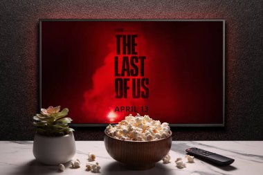 TV ekranında The Last of Us 2. Sezon fragmanı ya da film gösteriliyor. Uzaktan kumandalı televizyon, patlamış mısır kasesi ve ev bitkisi. Oyunun film uyarlaması. Astana, Kazakistan - 4 Nisan 2023.