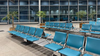 Geniş bir havaalanı bekleme salonu, boş sandalyeler büyük pencerelere bakıyor. Akşam havaalanı binasında boş bekleme sandalyeleri..