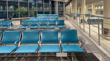 Geniş bir havaalanı bekleme salonu, boş sandalyeler büyük pencerelere bakıyor. Akşam havaalanı binasında boş bekleme sandalyeleri..