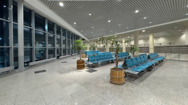 Geniş bir havaalanı bekleme salonu, boş sandalyeler büyük pencerelere bakıyor. Akşam havaalanı binasında boş bekleme sandalyeleri..