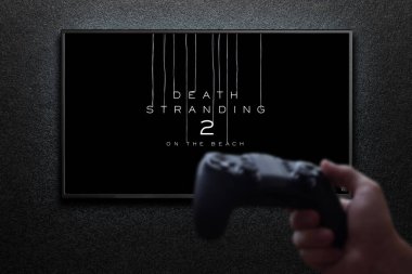 Death Stranding 2 - Televizyondaki plaj maçında, elinde av köpeğiyle siyah desenli duvarda ışıkla. Astana, Kazakistan - 26 Haziran 2025.