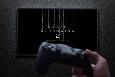 Death Stranding 2 - Televizyondaki plaj maçında, elinde av köpeğiyle siyah desenli duvarda ışıkla. Astana, Kazakistan - 26 Haziran 2025.