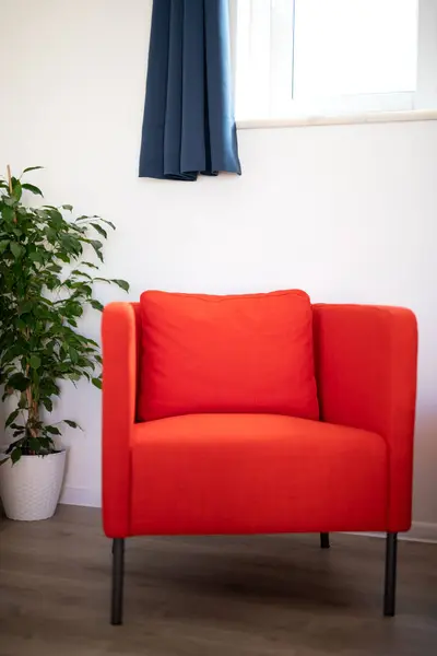 Red armchair in a home under a window and next to a potted plant