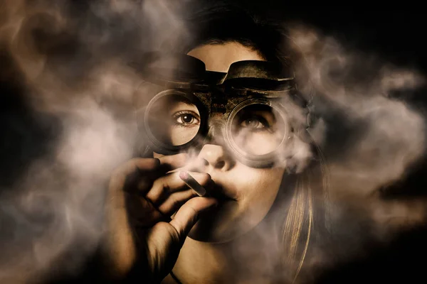 Creative art portrait on the face of a beautiful female mechanic smoking with industrial welding goggles in plumes of hot fumes. Steampunk welder