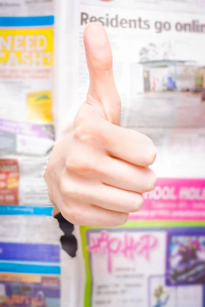 In Breaking News A Thumbs Up Hand Punches Through A Newspaper In A Symbol Of Good News Or Review Indicating A Positive Press Writeup