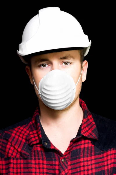 Headshot of a serious young male artisan wearing a hard hat and dust mask for particle inhalation protection on a black studio background