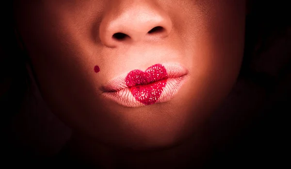 Closeup on the lips of a make-up model wearing heart shape glitter lipstick. Makeup love with a cosmetics kiss