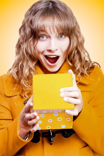 Excited bithday girl opening surprise gift with a look of amazement and shock in a Surprise Birthday concept on orange background