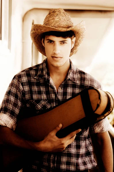 Country Music Man In Chequered Shirt And Straw Hat Heading West While Carrying A Guitar Case Under Arm