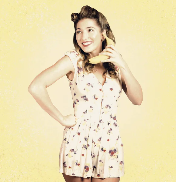 Forties popular culture portrait of a funny pin-up model making conversation through an imitation banana telephone in old fashion floral dress. Old-fashioned photographic advertisements