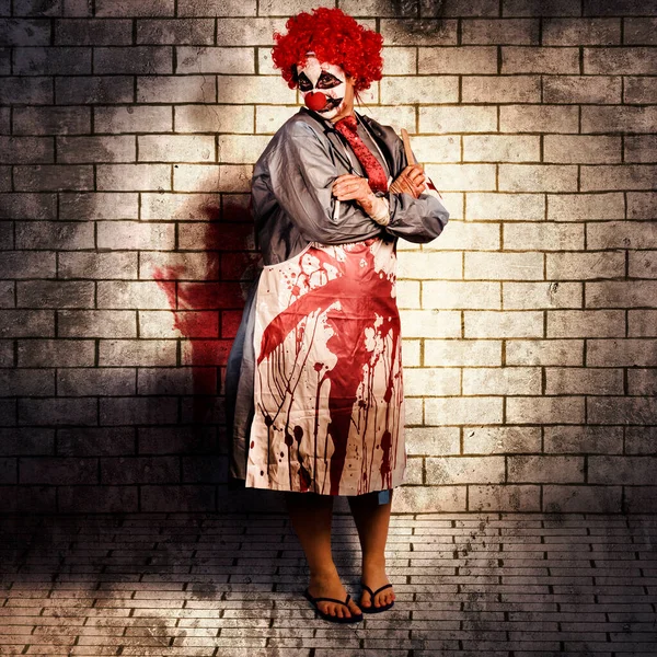 Murderous monster clown standing in full length on brick illustration background with blood stained apron. Killing medical practice