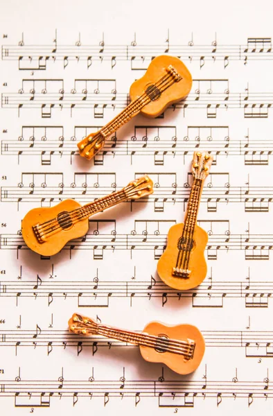 Quartet of four little country guitars on top of sheet music. Acoustic musical instruments
