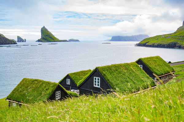 Village picture with traditional grass roof house and fjord landscape. Vagar, Faroe Islands.