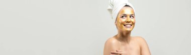 Yüzünde altın besleyici maske olan beyaz havluyla kadın portresi. Cilt temizleme eko organik kozmetik rahatlama konsepti.