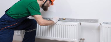 Erkek bir tesisatçı bir apartmanın ısıtma sistemine radyatör yerleştiriyor. Tulumlu ve ingiliz anahtarı olan bir adam..