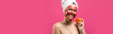 Kafasında kırmızı besleyici maske olan beyaz havluyla güzel bir kadın portresi. Cilt temizleme organik kozmetik rahatlama konsepti. Sırtı turuncu bir mandalina tutan bir kız..