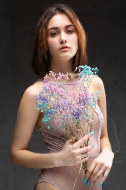 Zarif, çıplak bir beden giymiş güzel seksi bir bayan elinde çiçekler tutuyor. Moda mankeni kızın güzel portresi stüdyoda..