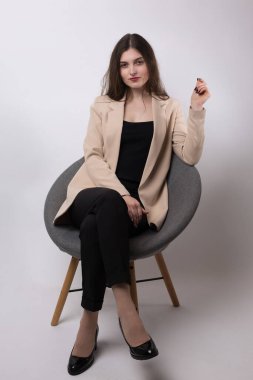 Stüdyoda uzun saçlı genç bir esmerin portresi. Beyaz arka planda sandalyede oturan tatlı kız..